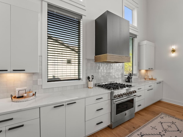 kitchen with wall chimney range hood, a wealth of natural light, white cabinetry, and stainless steel range