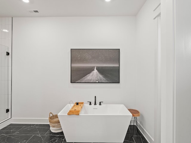bathroom with marble finish floor, baseboards, and a freestanding tub
