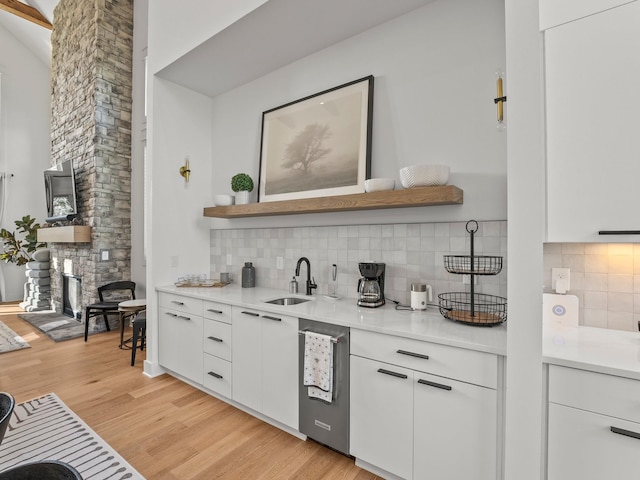 bar featuring backsplash, a sink, light wood finished floors, and a fireplace