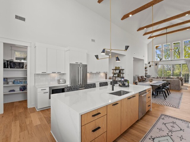kitchen featuring stainless steel appliances, high vaulted ceiling, a sink, beam ceiling, and open floor plan