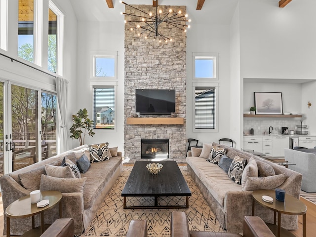 living room featuring a stone fireplace, a high ceiling, wood finished floors, and an inviting chandelier