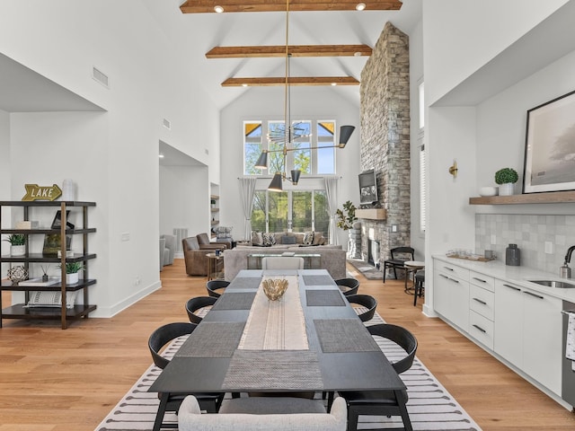 dining area featuring a stone fireplace, visible vents, light wood-style floors, beam ceiling, and high vaulted ceiling