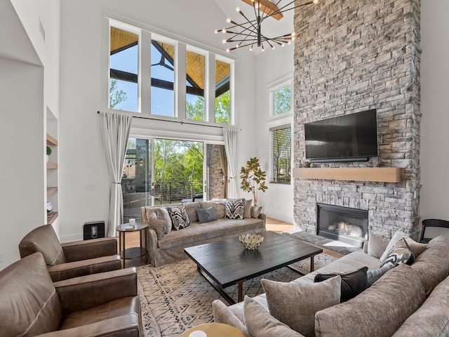 living room with a towering ceiling, an inviting chandelier, a stone fireplace, visible vents, and built in shelves