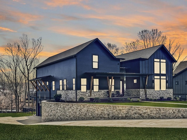 view of front of home featuring a front lawn, driveway, stone siding, a porch, and a garage