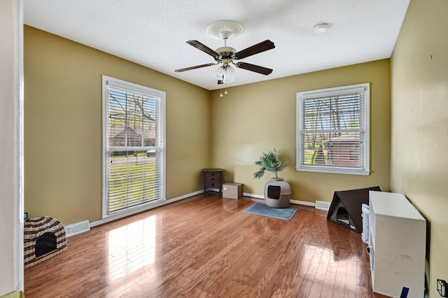 living area with ceiling fan, baseboards, wood finished floors, and a healthy amount of sunlight