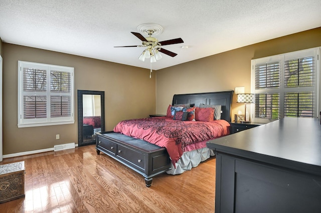 bedroom with light wood-type flooring, baseboards, visible vents, and a textured ceiling