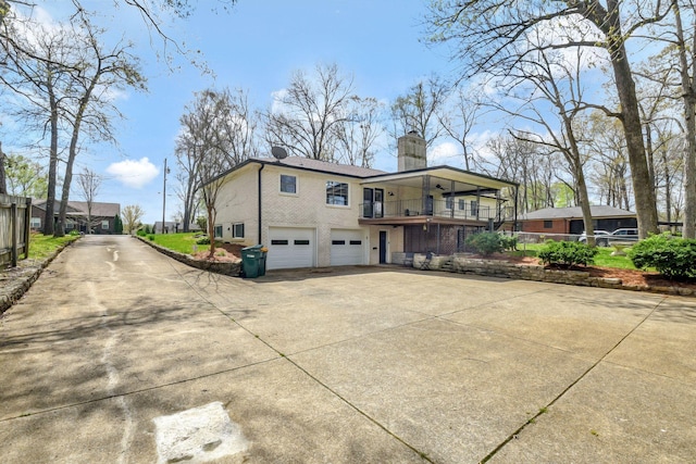 back of property with concrete driveway, brick siding, a chimney, and an attached garage