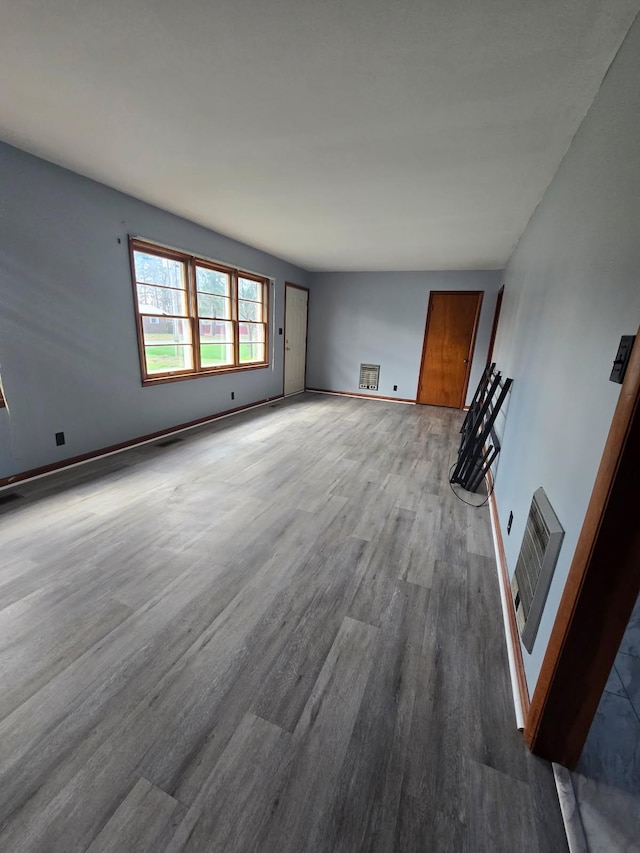 unfurnished living room featuring baseboards, heating unit, and wood finished floors