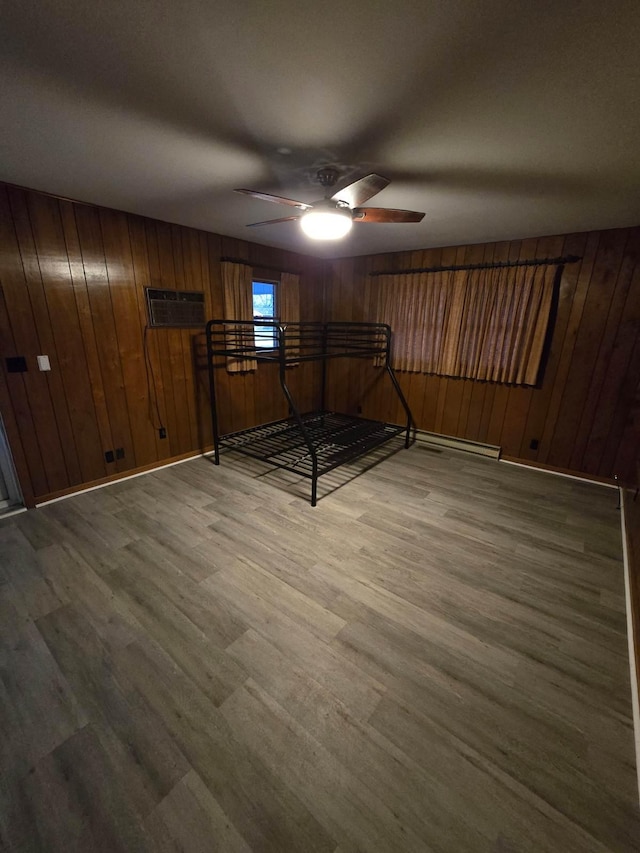 unfurnished bedroom with a ceiling fan, baseboards, wooden walls, and wood finished floors