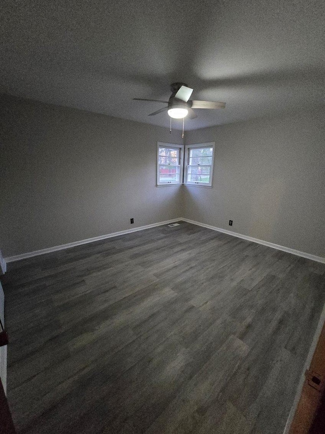 empty room with baseboards, a ceiling fan, and dark wood finished floors