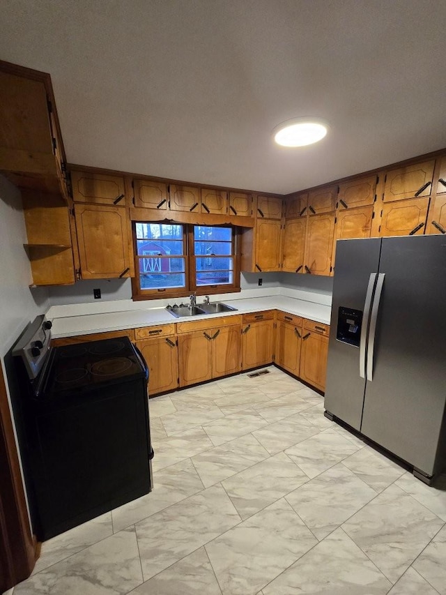 kitchen with brown cabinets, black electric range oven, a sink, and stainless steel refrigerator with ice dispenser