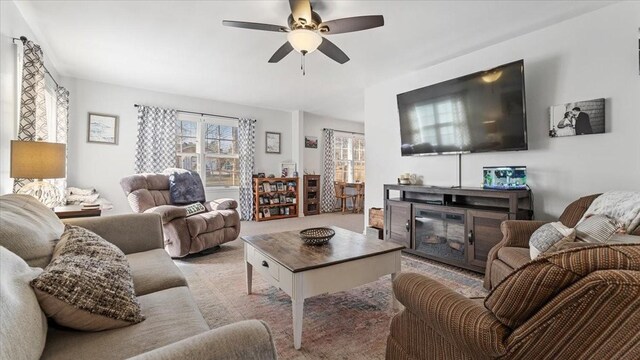 living area featuring a glass covered fireplace, a ceiling fan, and light carpet