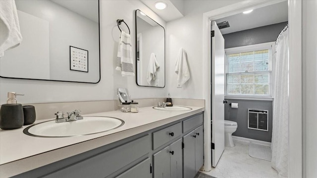 full bath featuring heating unit, double vanity, toilet, and a sink
