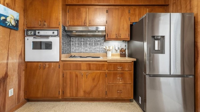 kitchen featuring light countertops, oven, under cabinet range hood, stainless steel fridge with ice dispenser, and brown cabinetry