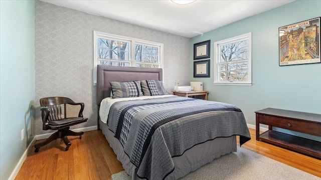 bedroom featuring wallpapered walls, baseboards, multiple windows, and wood finished floors