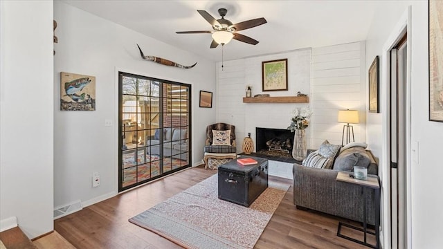 living area with visible vents, a fireplace with raised hearth, ceiling fan, and wood finished floors