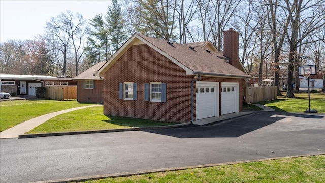 view of side of property featuring driveway, fence, a garage, brick siding, and a lawn