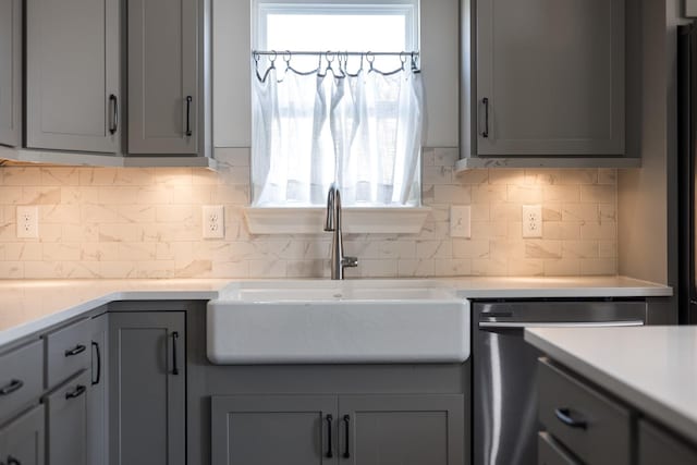 kitchen featuring light countertops, stainless steel dishwasher, a sink, gray cabinetry, and backsplash