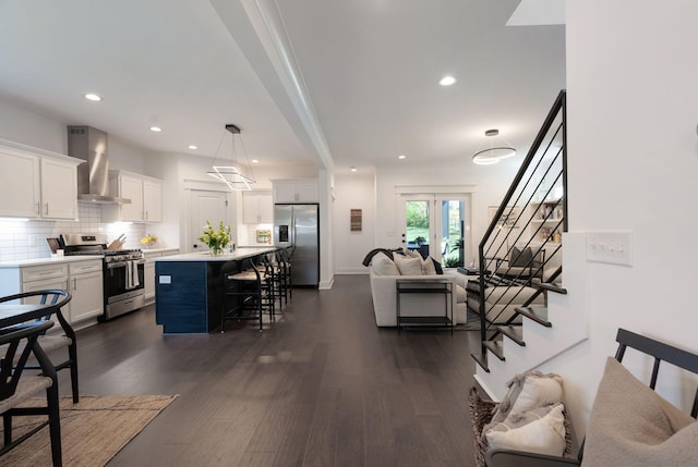 kitchen with appliances with stainless steel finishes, wall chimney exhaust hood, a breakfast bar area, open floor plan, and white cabinets