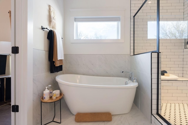 full bathroom featuring tile walls, a tile shower, a freestanding bath, and marble finish floors