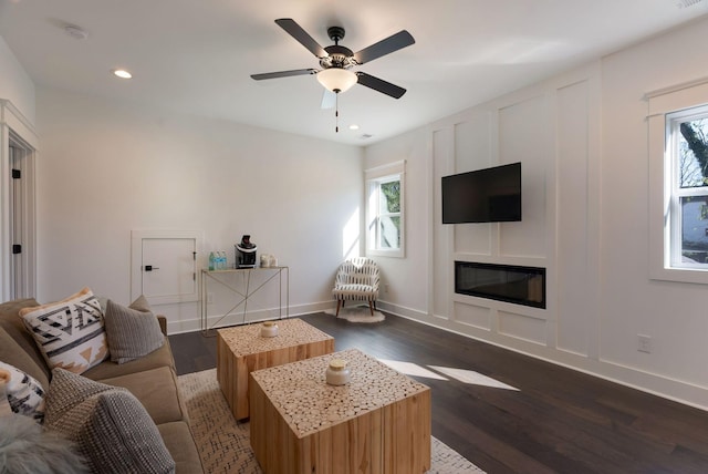living area with wood finished floors, a glass covered fireplace, recessed lighting, ceiling fan, and baseboards