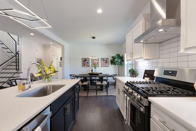 kitchen with stainless steel appliances, wall chimney exhaust hood, a sink, light countertops, and recessed lighting