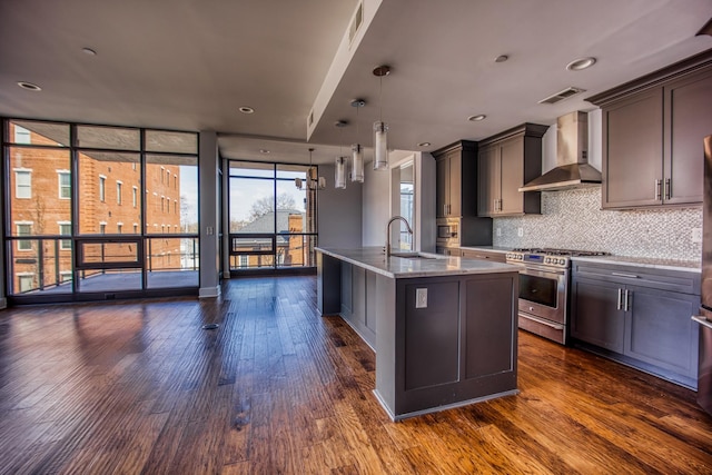3000 Poston Ave Unit 102, Nashville, TN 37203 - kitchen featuring backsplash, stainless steel gas range, dark wood-style floors, wall chimney range hood, and a kitchen island with sink