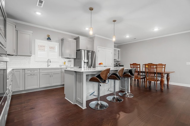 kitchen featuring crown molding, stainless steel fridge with ice dispenser, a breakfast bar area, backsplash, and visible vents