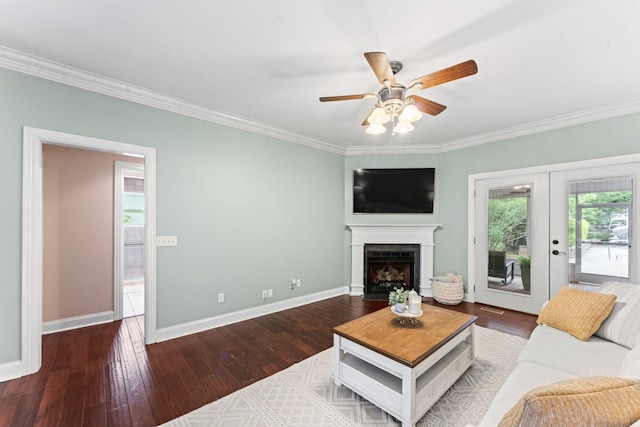 living area featuring a ceiling fan, a fireplace with flush hearth, wood finished floors, baseboards, and ornamental molding