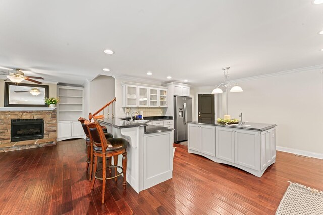 kitchen with dark countertops, a ceiling fan, glass insert cabinets, white cabinetry, and stainless steel fridge with ice dispenser