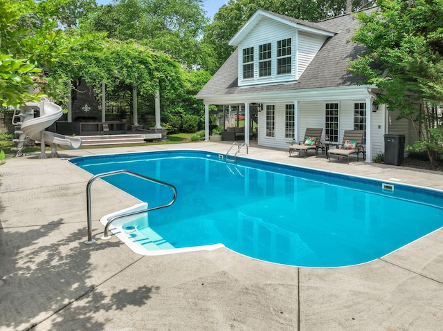 outdoor pool with a patio, an outbuilding, a water slide, and a storage structure