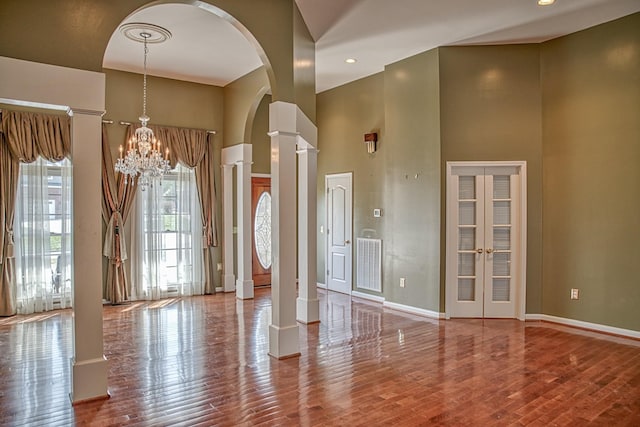 unfurnished dining area with visible vents, a towering ceiling, wood finished floors, decorative columns, and arched walkways