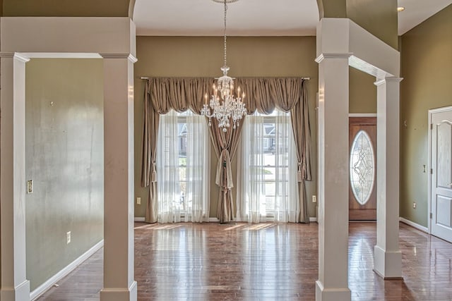 foyer with ornate columns, wood finished floors, a notable chandelier, and plenty of natural light