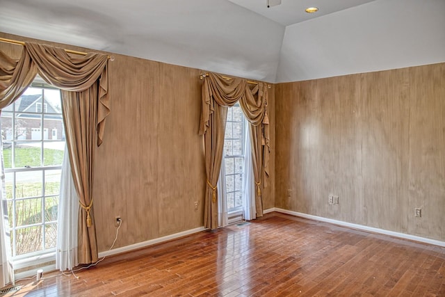 unfurnished room with a wealth of natural light, vaulted ceiling, and hardwood / wood-style flooring