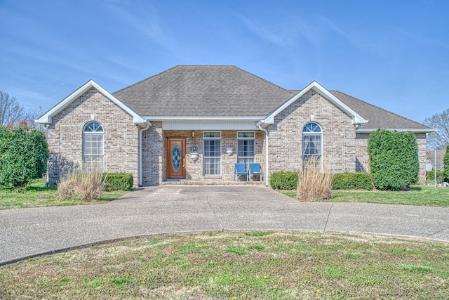 ranch-style house featuring roof with shingles, brick siding, and concrete driveway