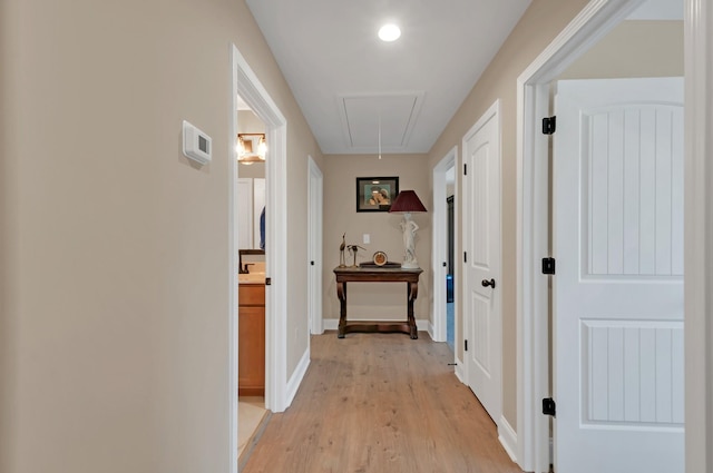 hall with attic access, baseboards, and light wood-type flooring