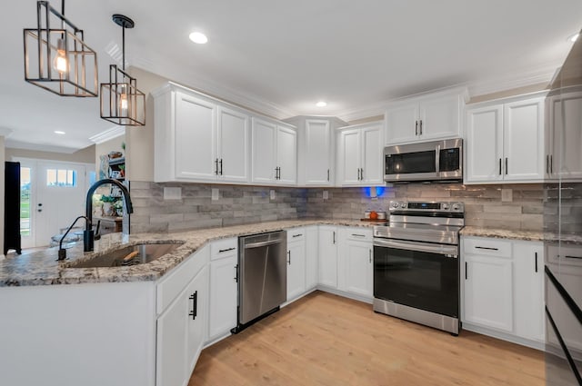 kitchen with a sink, appliances with stainless steel finishes, a peninsula, white cabinets, and ornamental molding