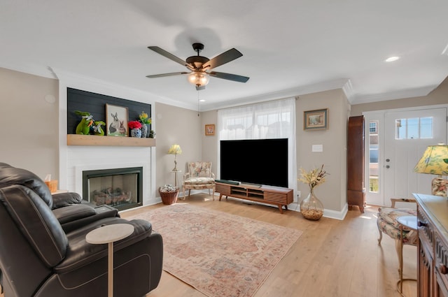 living room with light wood-type flooring, ornamental molding, baseboards, a ceiling fan, and a fireplace