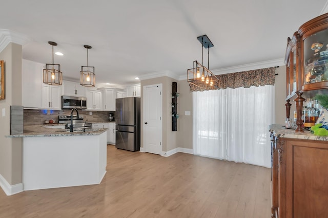 kitchen with light stone counters, appliances with stainless steel finishes, light wood-type flooring, white cabinets, and ornamental molding