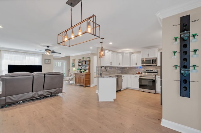 kitchen with white cabinets, stainless steel appliances, ornamental molding, and open floor plan
