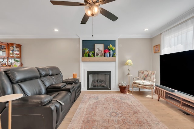 living room with a large fireplace, crown molding, light wood finished floors, ceiling fan, and recessed lighting