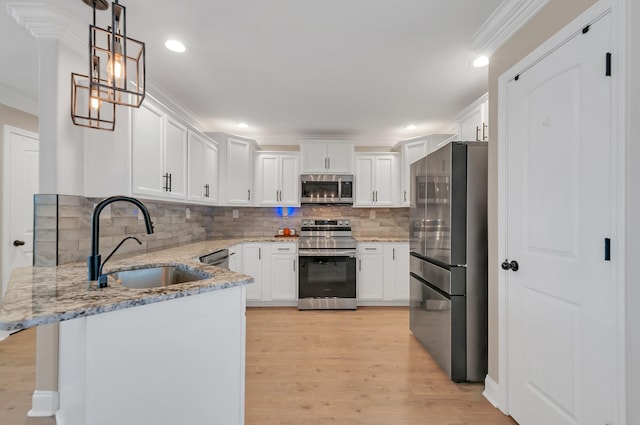kitchen featuring crown molding, stainless steel appliances, a sink, light wood-style flooring, and a peninsula