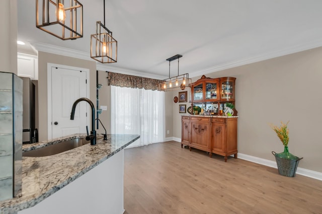 kitchen featuring baseboards, ornamental molding, a sink, light wood-type flooring, and light stone counters