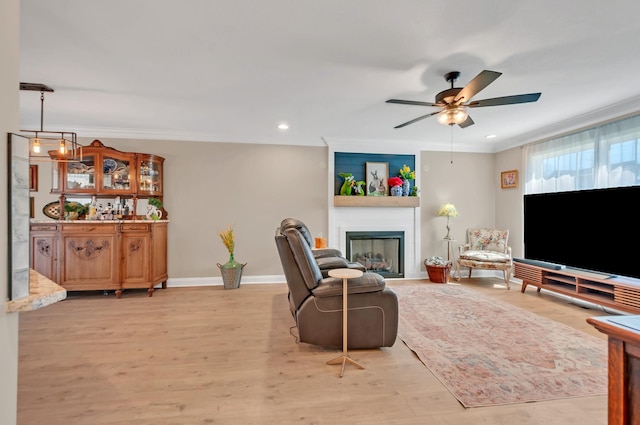 living area with crown molding, light wood-style flooring, and a ceiling fan