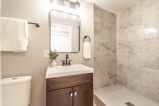 bathroom with toilet, tiled shower, and vanity