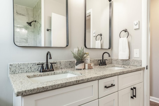 full bath with double vanity, a sink, baseboards, and a tile shower