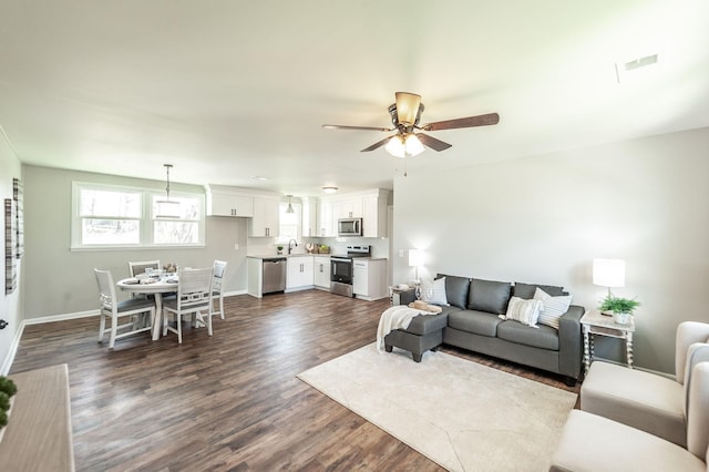 living room featuring dark wood finished floors, baseboards, visible vents, and ceiling fan