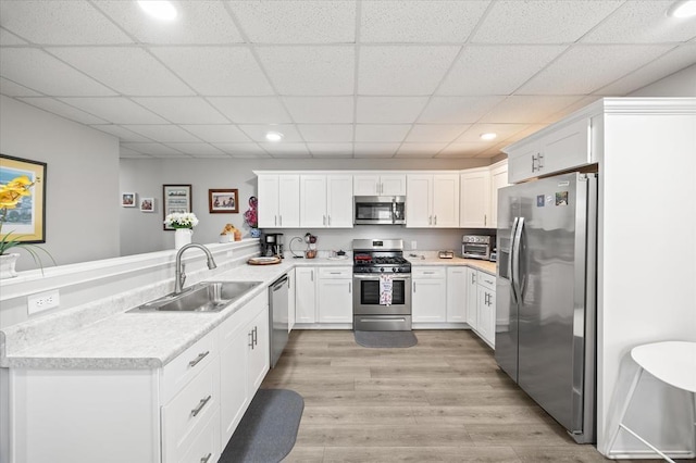 kitchen with light countertops, a peninsula, appliances with stainless steel finishes, a sink, and light wood-type flooring