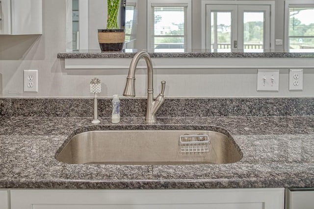 room details with white cabinetry, dark stone countertops, and a sink