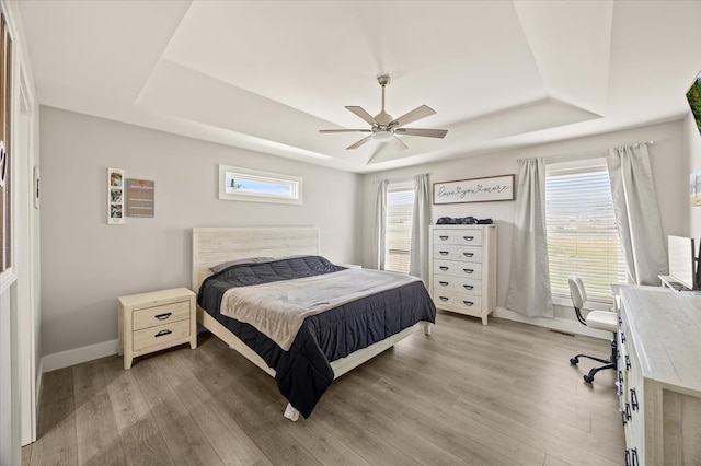 bedroom featuring baseboards, light wood finished floors, multiple windows, and a raised ceiling